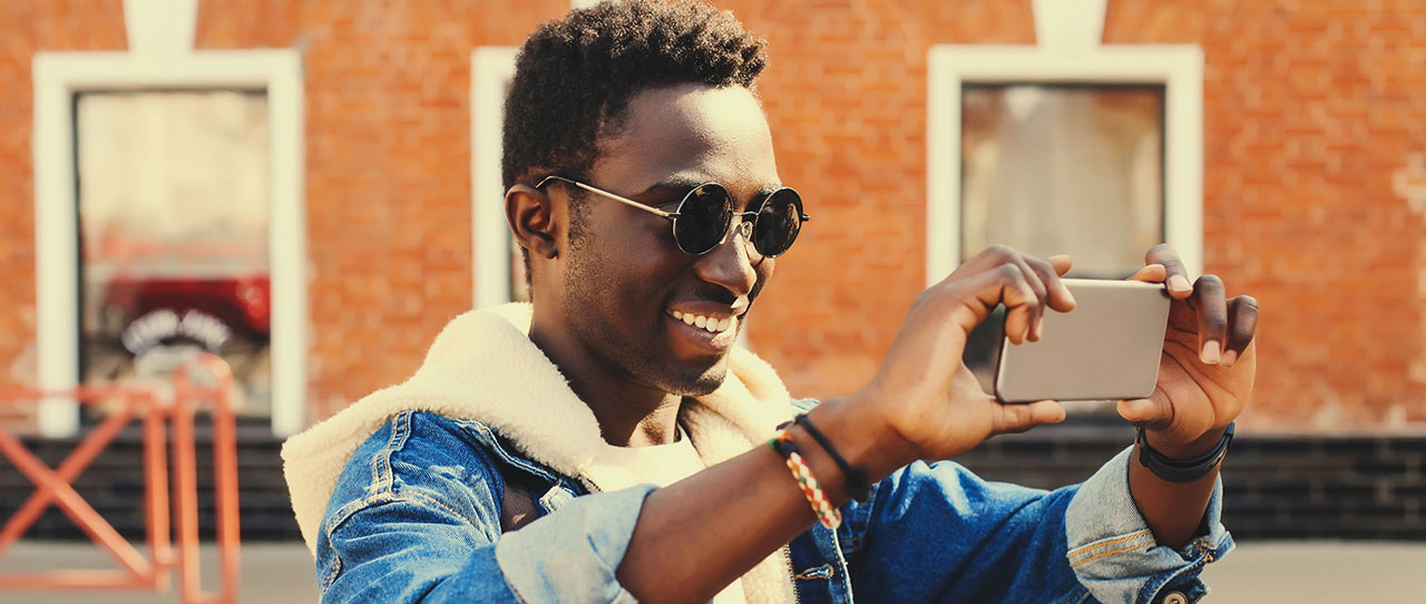 A young man in sunglasses taking a photo with his phone.